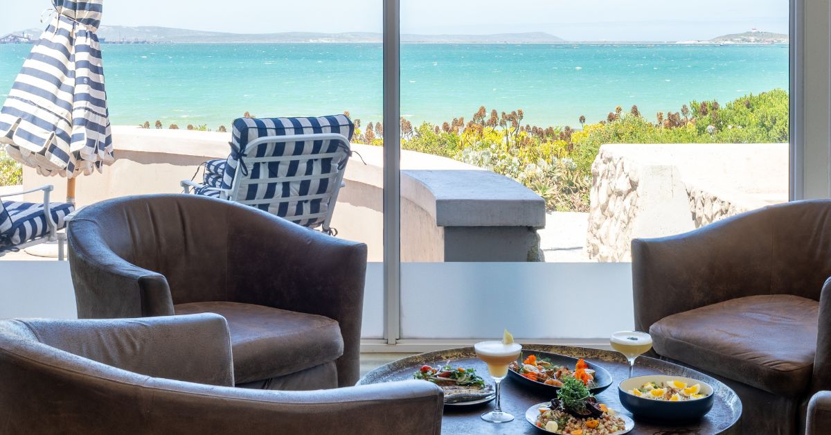 A lounge with drinks and food on a table with the ocean in the distance
