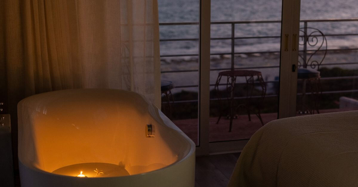Winter getaways western cape feature image- Close up of a cosy bathtub with a candle in it, overlooking the ocean
