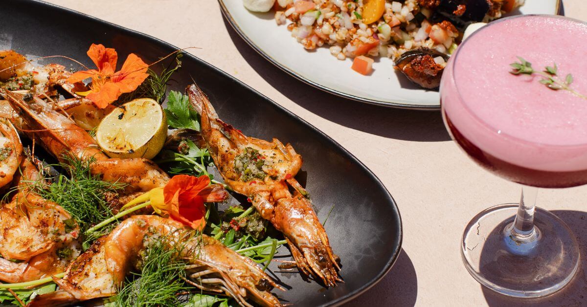 Prawns on a plate and a pink cocktail at The Bay Club and Social