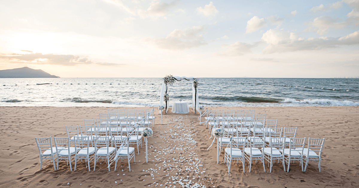 Beach wedding ceremony setup with white chairs and floral arch overlooking the ocean